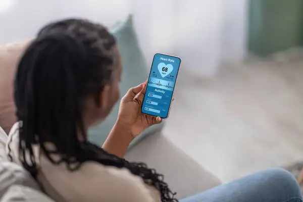 Kobieta sprawdza na telefonie swoje skoki tętna i aktywność fizyczną. Widzi 68 uderzeń na minutę, spalone kalorie i pokonane kroki.