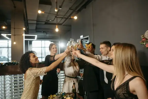Grupa ludzi w eleganckich strojach na uroczystą kolację firmową wznosi toasty szampanem.