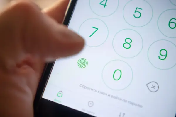 Zbliżenie na ekran telefonu z klawiaturą numeryczną, ikoną odcisku palca i palcem wskazującym.