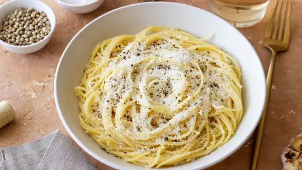 Miseczka spaghetti posypana parmezanem i pieprzem, obok przyprawy i czosnek.