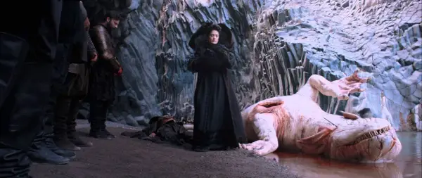 Una donna in nero osserva un mostro acquatico morto, con guerrieri al fianco. Scena da "Il racconto dei racconti recensione".
