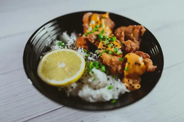 Chrupiące karaage z ryżem, posypane sezamem i szczypiorkiem, podane z plasterkiem cytryny.