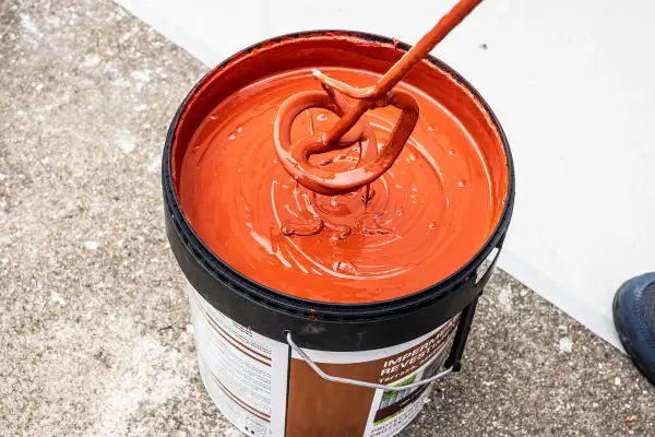 Mezclando pintura impermeabilizante naranja en un cubo. El tiempo secado pintura impermeabilizante es clave para un buen acabado.