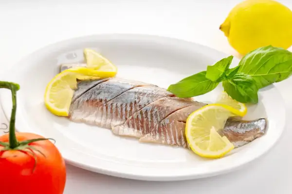 Filety śledzi z cytryną i bazylią na talerzu. Kto nie powinien jeść śledzi? Alergicy i osoby z problemami z cholesterolem.