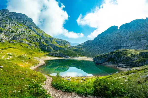 Sentiero panoramico verso un lago alpino turchese, incorniciato da montagne maestose. Un vero gioiello dell'alta via Dolomiti più bella.