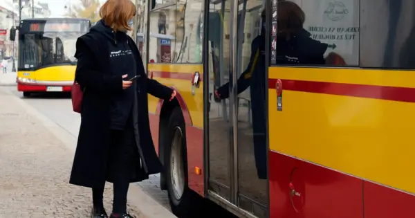 Kobieta z telefonem w ręku zbliża się do autobusu, by skasować bilet elektroniczny.