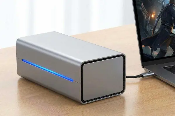Srebrna obudowa egpu do laptopa z niebieskim podświetleniem, podłączona do laptopa z grą na ekranie.