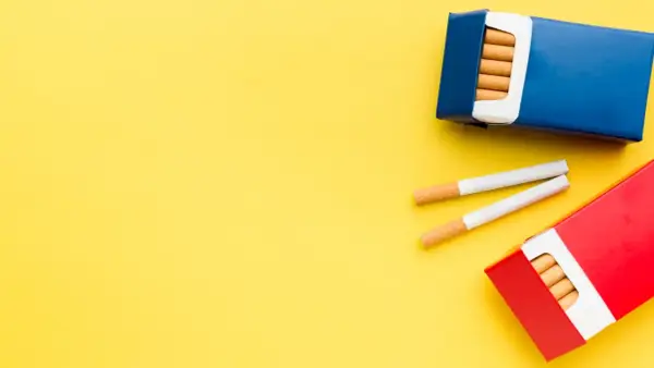 Dwie paczki papierosów, jedna niebieska, druga czerwona, leżą na żółtym tle. Dwa papierosy leżą obok. Ile papierosów do Niemiec?