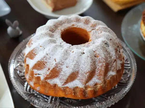 Puszysta babka drożdżowa, jak z babcinego przepisu, oprószona cukrem pudrem, na kryształowej paterze.