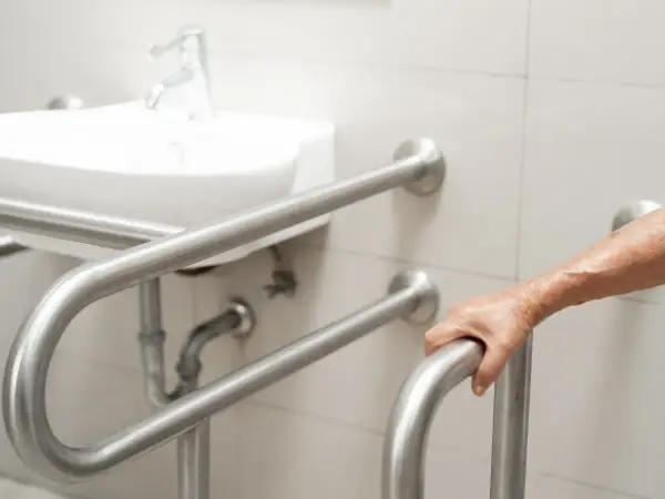 Dłoń osoby starszej chwyta uchwyt dla niepełnosprawnych. Łazienka przystosowana zgodnie z przepisami.