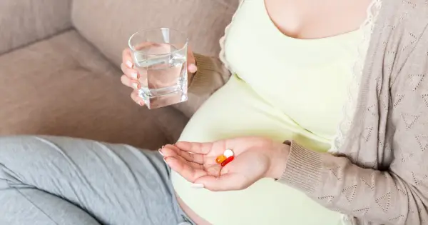 Kobieta w ciąży bierze suplementy, w tym magnez, popijając wodą. Dba o zdrowie swoje i dziecka.