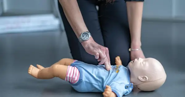 Ćwiczenie reanimacji a resuscytacji niemowlaka na fantomie. Dłoń instruktora uciska klatkę piersiową.