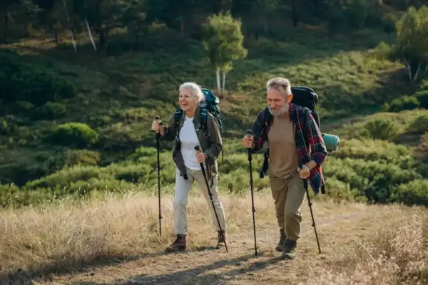 Uśmiechnięta para seniorów z plecakami przemierza leśny szlak, ucząc się, jak chodzić z kijkami.