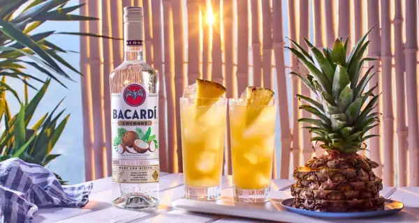 Butelka Bacardi Coconut obok dwóch drinków z ananasem i cała ananasowa piramidka. Idealne na tropikalne przyjęcie!