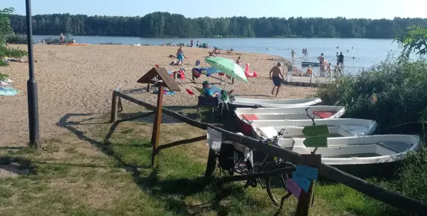 Słoneczny dzień nad zalewem zielona. Ludzie odpoczywają na plaży, kąpią się w wodzie, a obok cumują łódki.