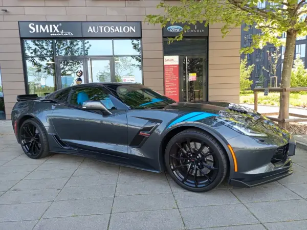 Szary Chevrolet Corvette C7 z niebieskimi pasami, zaparkowany przed salonem samochodowym. Sprawdź aktualną corvette c7 cena!