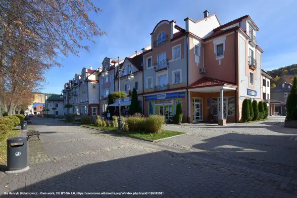 Urokliwy rynek w Ustrzykach Dolnych z kolorowymi kamienicami, zielenią i brukowanym deptakiem.