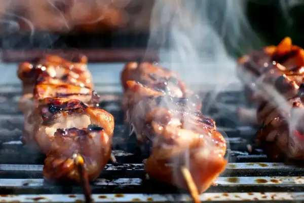 Aromatyczne yakitori skwierczy na grillu, otoczone kłębuszkami dymu.