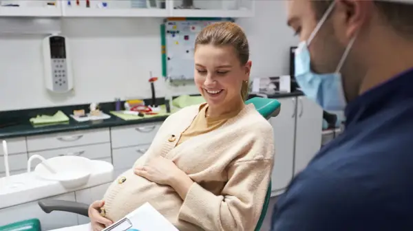 Donna incinta sorride dal dentista, preoccupata per la carie in gravidanza.