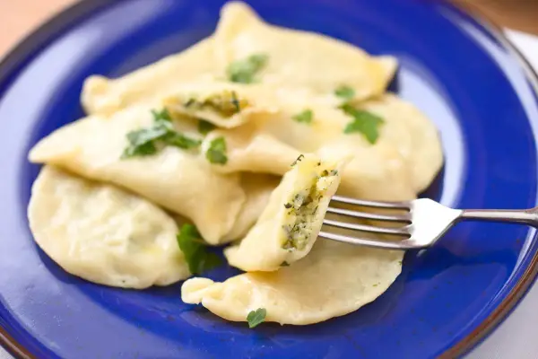 Pyszne pierogi ze szpinakiem i serem feta, udekorowane natką pietruszki, czekają na widelcu.
