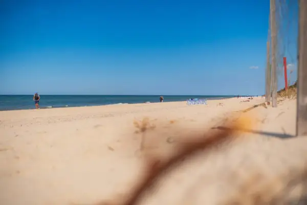Słoneczna plaża w Niechorzu, idealne miejsce na relaks. W oddali widać ludzi spacerujących brzegiem morza.