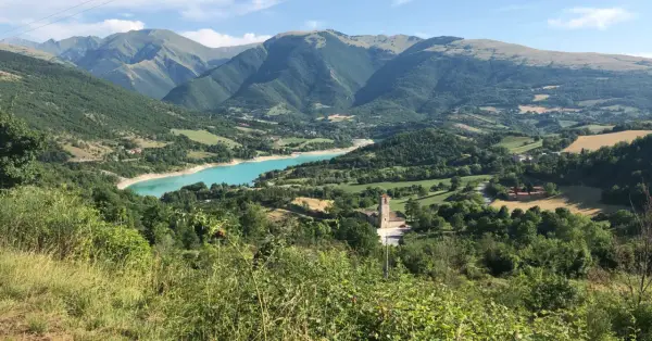Panoramica del lago di Fiastra, con montagne verdi, un borgo e una chiesa. Cosa vedere in questo paesaggio mozzafiato.