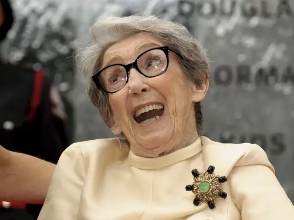 Uśmiechnięta babcia po francusku, w okularach i eleganckiej broszce, z otwartymi ustami.