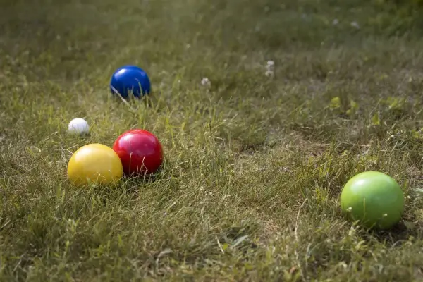 Boules colorées (jaune, rouge, bleu, vert) et une petite blanche sur l'herbe, prêtes pour un concours de pétanque.