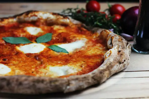 En perfekt pizza på grillen, med smält mozzarella och färsk basilika. Tomater och vitlök i bakgrunden.