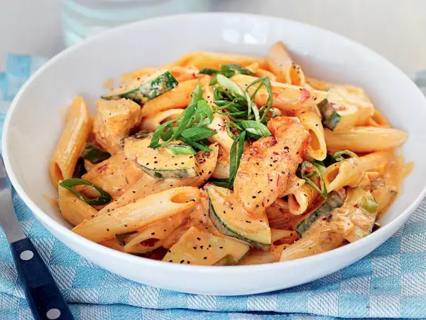 En skål med krämig penne med kyckling och zucchini, toppad med salladslök. En riktigt god pasta!