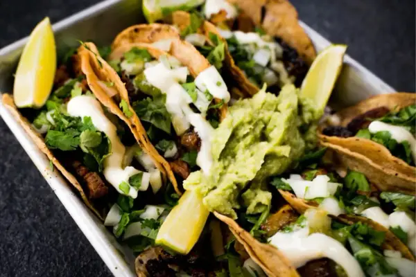 Saftige Tacos al Pastor mit Guacamole, Koriander und Limettenspalten.
