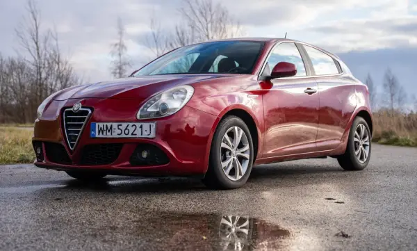 Czerwone Alfa Romeo Giulietta na mokrej drodze. Wiele osób szuka alfa romeo giulietta opinie przed zakupem.