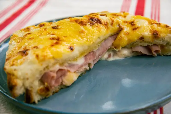 Croque Monsieur gratinado con queso derretido y jamón, servido en plato azul.