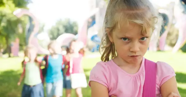 Zagniewana dziewczynka, bunt 7 latka, na tle bawiących się dzieci i placu zabaw.