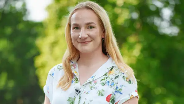 Uśmiechnięta Klaudia, uczestniczka "Rolnik szuka żony", w kwiecistej koszuli na tle zieleni.