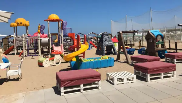 Area giochi per bambini sulla sabbia, con scivoli, altalene e piscina di palline. Un angolo di divertimento al Regina Beach Cattolica.