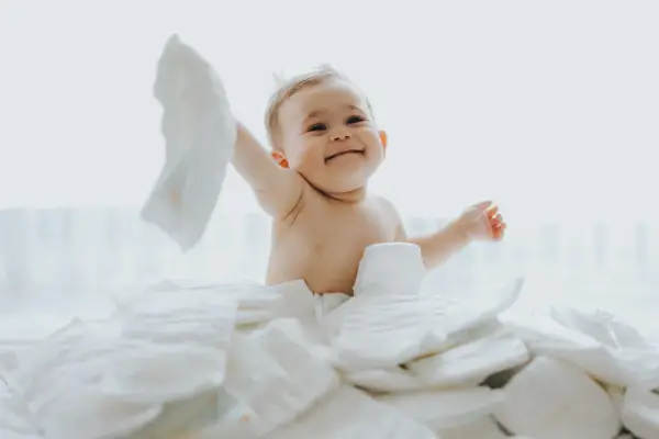 Uśmiechnięty bobas otoczony stertą pieluch. Zastanawiasz się, jakie pieluchy dla noworodka będą najlepsze?