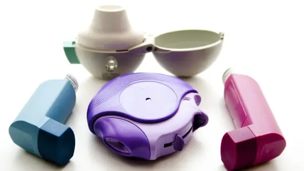 Drei Inhalatoren in Lila, Blau und Pink, sowie ein offener weißer Inhalator. Ein Beispiel für Medikamente wie Spiriva.