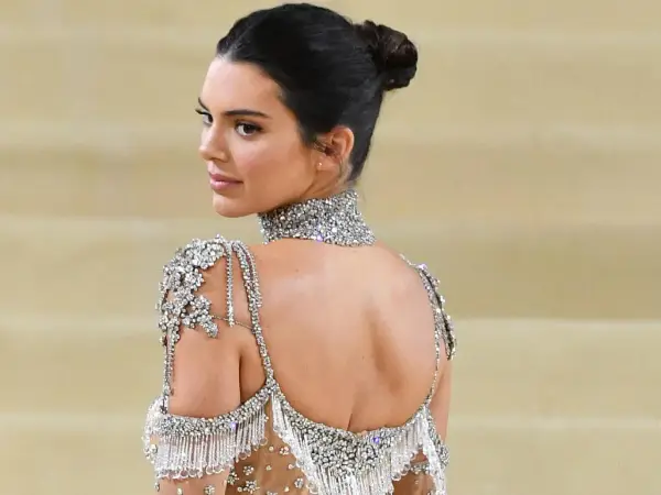 Mujer con un elegante moño recogido, luciendo un vestido de pedrería y un collar brillante.