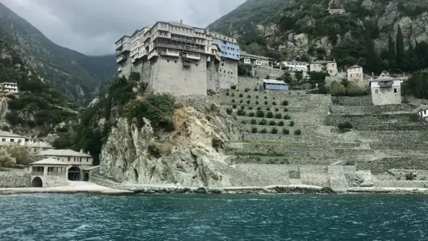 Monastyr na Athos, zbudowany na skalistym zboczu, z tarasowymi ogrodami i widokiem na morze.