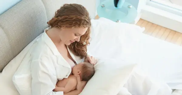Matka karmi piersią swoje 6 miesięczne dziecko w łóżku.