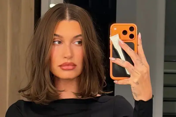 En kvinna med fina hårfrisyrer tar en selfie med sin orangea mobil.