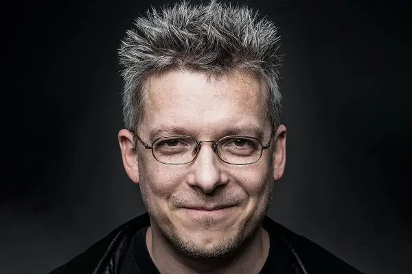 Uśmiechnięty mężczyzna w okularach, z siwymi, nastroszonymi włosami. Może to być jeden z bohaterów Felix Net i Nika, gotowy na przygodę.