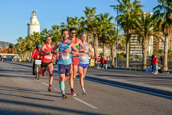 Läufer im Malaga Marathon kämpfen sich unter Palmen durch. Ein Leuchtturm im Hintergrund.