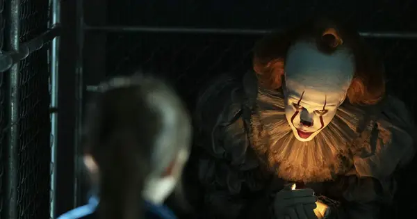 Przerażający klaun Pennywise z "To" w jednym z najlepszych horrorów ostatnich lat, świeci sobie zapalniczką.