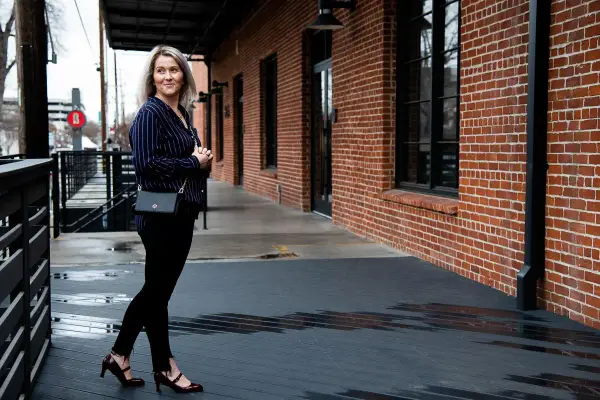 Mujer con outfit de camisa azul a rayas, pantalones negros y zapatos de tacón.