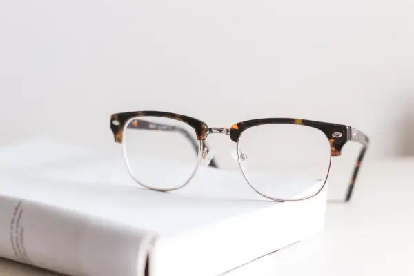 Okulary z oprawkami w stylu clubmaster leżą na białej książce. Czy wada 0.75 to powód, by nosić okulary?