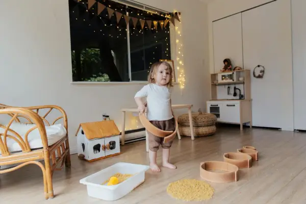 Dziecko bawi się w pokoju inspirowanym 10 zasadami Montessori. Drewniane zabawki, domek i kuchnia zachęcają do samodzielnej nauki.