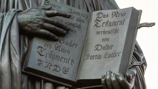 Hände halten ein aufgeschlagenes Buch mit Luthers Übersetzung des Neuen Testaments. Die Bedeutung der Reformation wird durch diese Darstellung greifbar.