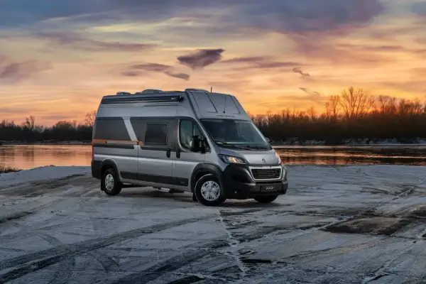 Srebrny kamper Globe-Traveller na tle zachodzącego słońca nad rzeką. Idealny wybór, jeśli zastanawiasz się, jaki kamper dla 2 osób sprawdzi się najlepiej na zimowe wyprawy.